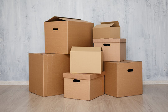 moving day concept  - brown cardboard boxes with belongings stacked over gray wall
