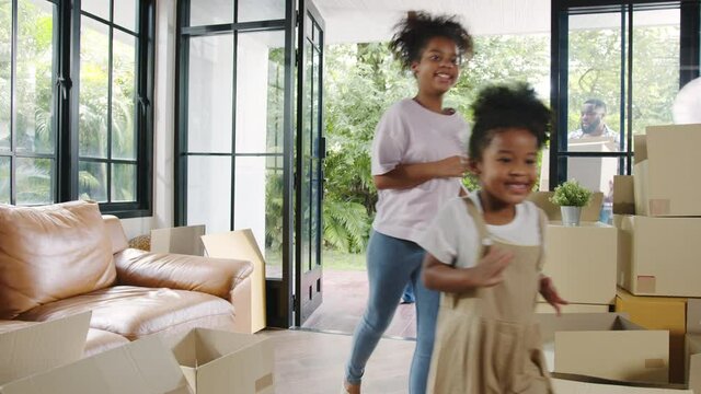 Happy African American young family bought new house. Mom, Dad, and child happy hold cardboard boxes for move object and having fun laugh into modern home. New real estate dwelling, loan and mortgage.
