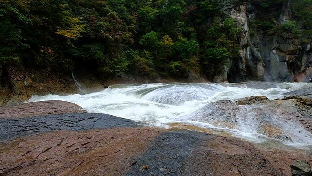 A slow motion of a large water stream that flows noisily in a huge rocky environment, Fukiware Falls, next to Numata, near Nikko National Park, Japan.
