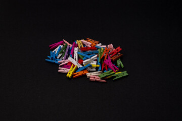 Colored wooden clothes pins on a pile in middle of black background, colorful banner with copy space