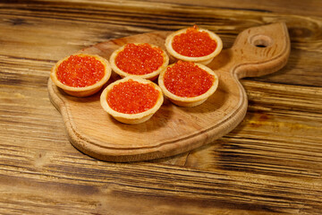 Tartlets with red caviar on a wooden table