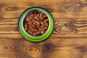 Canned food for cats or dogs in green metal bowl on wooden floor. Top view