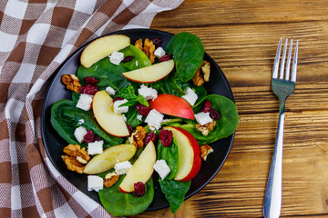 Autumn spinach salad with apple, feta cheese, walnut and dried cranberry on wooden table. Top view. Healthy vegetarian food