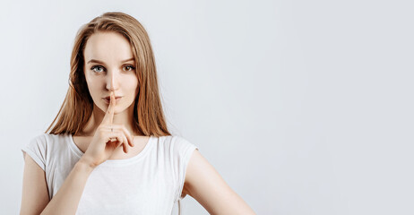 Young beautiful girl smiling and showing finger hush gesture on gray isolated background