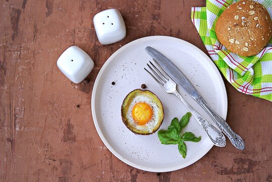Light healthy breakfast or lunch, egg, baked in half a ripe avocado on a white ceramic plate.