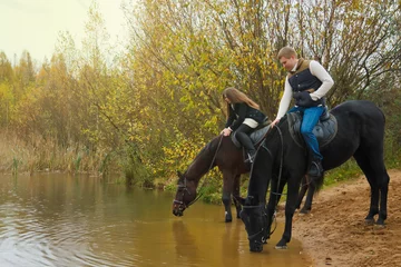 Foto op Canvas Cute young couple on horseback in the autumn forest by lake. Horses drink water in pond, people stroke their manes. Rider in autumn Park. Concept of outdoor riding, sports and recreation. Copy space © Alex Vog