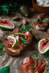 Fototapeta na wymiar Bruschetta with prosciutto ham, ricotta cheese and fresh figs on a sheet of paper. appetizing appetizer. Selective focus, close-up. Food party concept