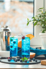Two glasses of blue gin tonic cocktail with ice a mix of alcohol near the window on the table near window in the sun falltime. Real life in new reality in under quarantine