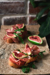Bruschetta with prosciutto ham, ricotta cheese, arugula and fresh figs on a dark paper background. Appetizing appetizer, starters concept. Selective focus, shallow depth of field