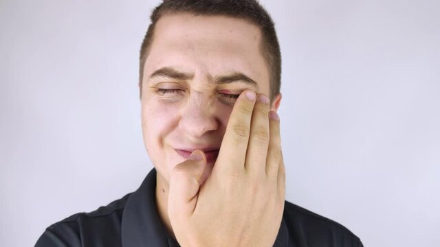 A man stands in front of a mirror and sees inflammation of the upper eyelid. Redness of the skin around the eyes and blepharitis.
