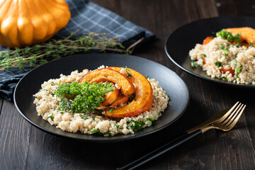Roasted pumpkin salad with quinoa, kale and pine nuts in a black plate on wooden background