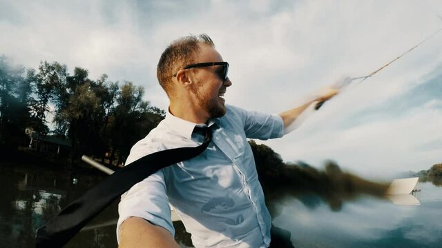 Selfie on action camera of extreme businessman in a suit with a tie and sunglasses rides on wakeboard on a lake at sunset at the end falls under the water..