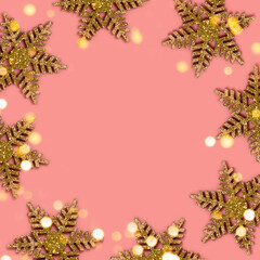 Frame made of golden shimmer snowflakes on a coral background. Shiny festive concept with copy space.