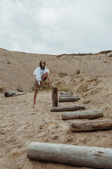 Picturesque sand pit with wooden logs and a tiny fashion model posing in a stylish outfit.