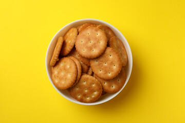 Wooden bowl with tasty cracker biscuits on yellow background