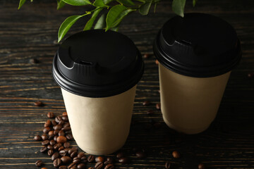 Paper cups, coffee beans and plant on wooden background