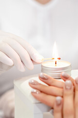 Fototapeta na wymiar Manicure master in white gloves lighting candle with match in nail salon