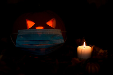 Jack o lantern medical face mask candle on adark and yellow maple leaves background and with dry leaves,