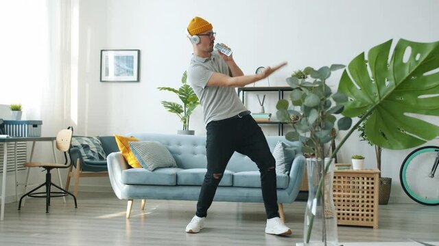Carefree guy is dancing and singing listening to music through headphones relaxing at home enjoying life alone. Emotions and modern lifestyle concept.
