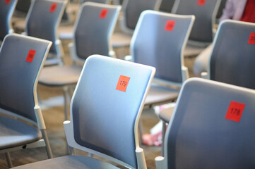 A row of empty light blue chairs, selective focus on a seat with number 179 that written on a small...
