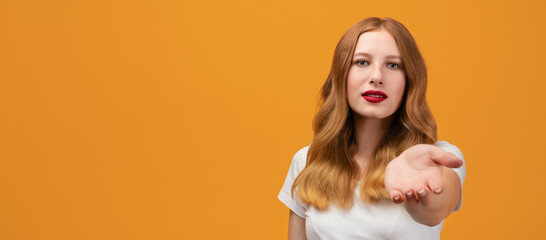 Pretty girl with long wavy redhead, smiling offering palm of hand at camera. Copy space