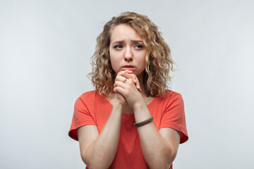 Portrait of brunette dressed in casual red sweater keeping hands together near chin. Studio shot, white background