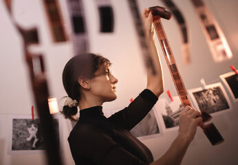 Young creative female holding filmstrip. Portrait of creative girl photographer in photo studio darkroom. Developing analog camera film
