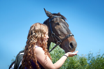 Obraz premium Fat girl with long curly hair with brown horse outdoors on a Sunny day.