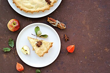 Sliced traditional round homemade American apple pie on a ceramic plate on a brown concrete background. Thanksgiving Day. Baking apples. American cuisine.