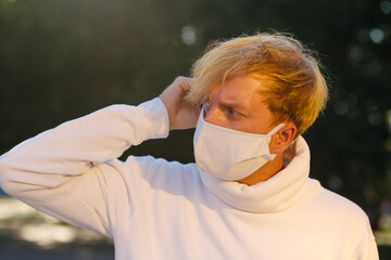 A young man in a medical protective mask, anxiously looking to the side, adjusting the mask.