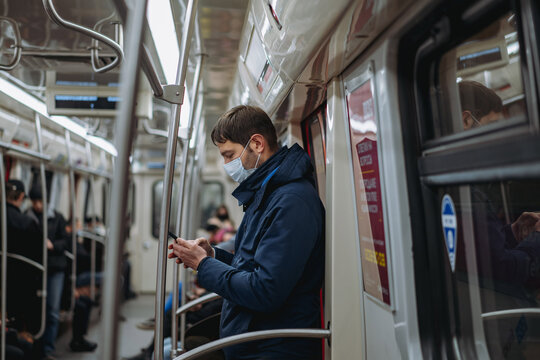 caucasian man wearing medicine mask traveling by tube, standing in subway car holding mobile telephone in hands.Image with selective focus