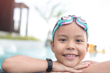 smiling child wearing swimming glasses in swimming pool. little girl playing in outdoor swimming pool on summer vacation on tropical beach island. child learning to swim in pool of luxury resort.