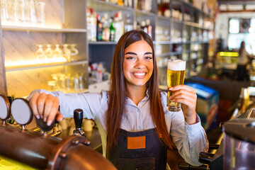 Beautiful smiling female Bartender serving a draft beer at the bar counter , shelves full of...