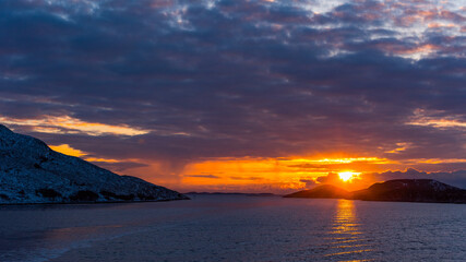 Glorious sunset over norwegian coast with snow covered rocks and dense clouds seen from open sea