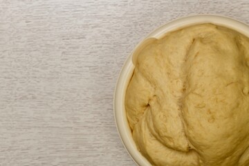 Fragment of the bowl with a raised fermented yeast dough. On the table.