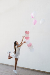 Fototapeta premium Woman with hearts and pink air balloons on bachelorette party outdoors. Beautiful sexy young girl in dress and veil on bachelor party. Maiden evening, Hen-parties. Place for text.