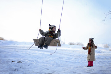 Fototapeta na wymiar Smiling girl and her little brother flying on a swing in winter