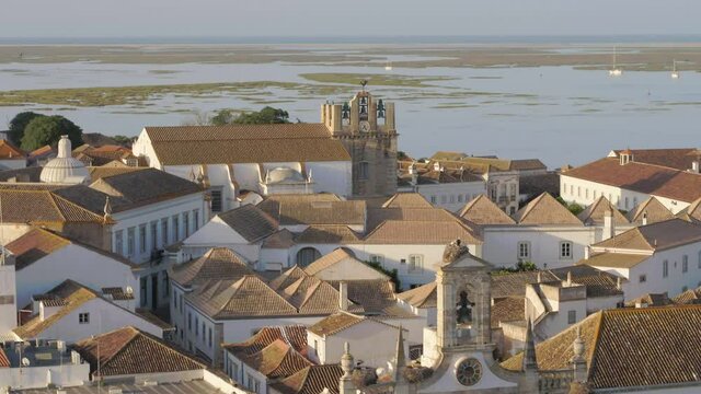 Drone flies over the old Traditional European village in Faro, Portugal, revealing oceanside rooftops and Church steeple, Aerial