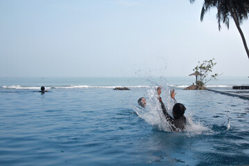 Joyful brothers playing water splash on the infinity pool with sea view on the background