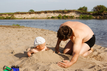 child with dad playing on the beach by the water