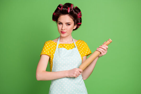 Photo of attractive cunning lady curlers hairdo housewife hold wooden rolling pin ready start bake cake addicted cooking wear pinup dotted dress apron isolated green color background