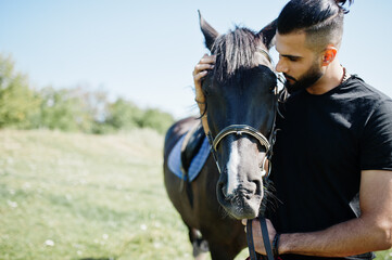 Arab tall beard man wear in black with arabian horse.