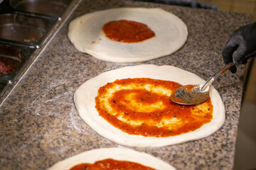 chef pizza with a metal spoon spreads tomato sauce on the dough in gloves. copy space