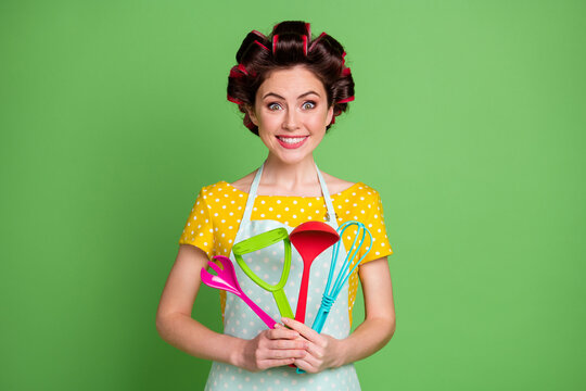 Photo of positive cheerful girl hold spatula spoon fork potato masher whisk enjoy prepare recipe wear good look clothes isolated over green color background