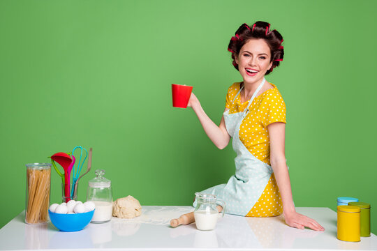 Photo housewife chef girl enjoy cook prepare pizza rest relax drink coffee mug beverage sit table wear yellow stylish trendy dotted skirt dress hair rollers isolated green color background