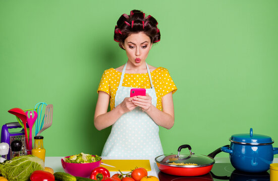 Photo of shocked girl prepare fresh dish use smartphone choose recipe table with pepper salad tomato wear yellow dotted t-shirt hair rollers isolated green color background
