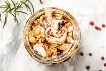 Cheese pieces with herbs and spices in olive oil in a glass jar on a light background, top view