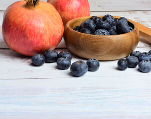 Blueberries and pomegranates on a white table, next to kitchen utensils made of wood.