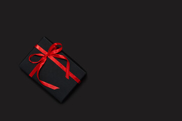 Black Friday sale concept. Black gift with red ribbon and bow on dark background. Holiday template...