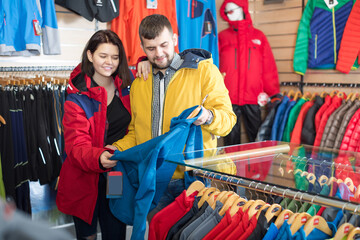 Young loving couple deciding on track jacket in sports clothes store